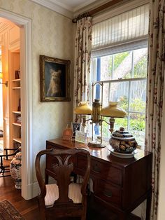 a room with a desk, chair and lamp on it in front of a window