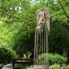 a statue of an angel is in the middle of a park with trees and bushes