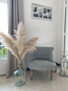 a living room with a chair and vase filled with dry grass next to a window