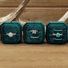 three rings are sitting in velvet cases on a wooden table next to antelope