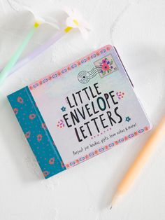 the little envelope letters book is next to two pencils and an eraser on a white surface