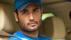 a man sitting in the back seat of a car wearing a blue shirt and hat