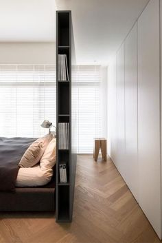 a book shelf in the corner of a bedroom next to a bed with pillows on it