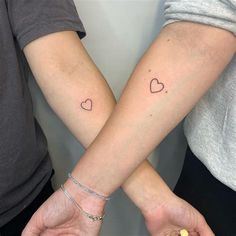 two people holding hands with small hearts on their wrist tattooing one another's arm