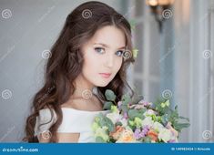 a beautiful young woman holding a bouquet of flowers in her hand and looking at the camera