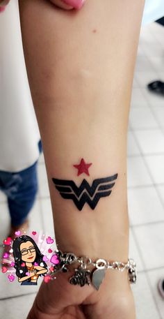 a woman's arm with a tattoo on it and a wonder girl charm attached to the wrist