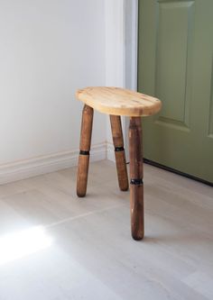 a wooden stool sitting on top of a hard wood floor next to a green door