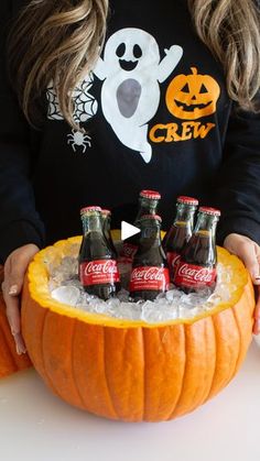 a woman holding a carved pumpkin with six bottles in it and ice on the bottom