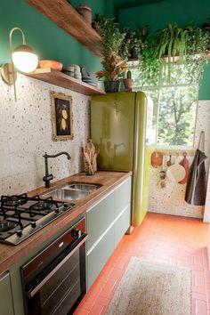 a kitchen with green walls and red tile flooring is pictured in this image, there are potted plants on the shelves above the stove