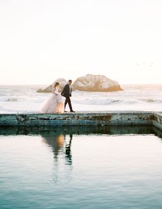 a bride and groom are walking along the pier by the water at their beach wedding