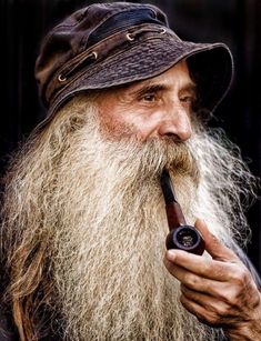 an old man with a long beard is holding a pipe in his right hand and wearing a hat