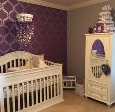 a white crib and dresser in a room with purple wallpaper on the walls