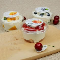 three desserts in plastic containers on a cutting board with cherries and strawberries