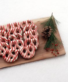 candy cane donuts are arranged on a cutting board next to a pine cone and evergreen branch