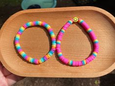 a wooden tray holding two colorful bracelets on it's side, with a smiley face in the middle