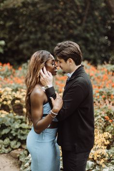 a man and woman standing next to each other in front of some bushes with orange flowers