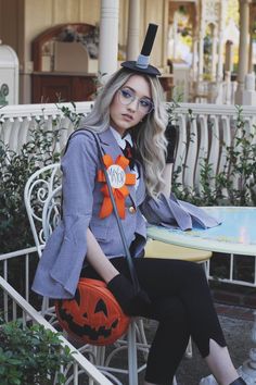 a woman sitting on top of a chair wearing a hat and holding a pumpkin bag