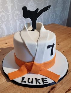 a cake that has a karate figure on top and an orange ribbon around the edge