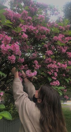 a woman reaching up to pick flowers from a tree