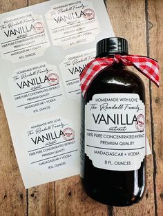 a bottle of vanilla syrup next to some stickers on a wooden table with a red and white checkered ribbon