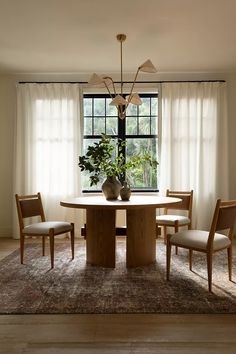 a dining room table with four chairs and a vase on the table in front of a window