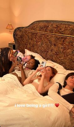 four women laying in bed taking pictures with their cell phones and camera phone cameras,