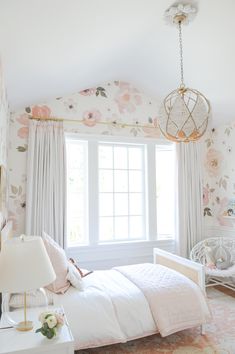 a white bed sitting under a window next to a lamp on a table in a bedroom