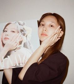 a woman holding up a magazine with her hand on her face and looking at the camera