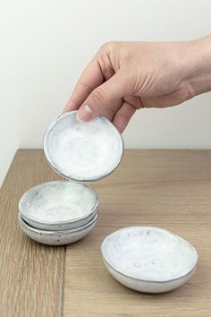 a person is picking up some food from two white bowls on a table with another bowl in the background