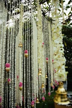 white and pink flowers are hanging from the ceiling in front of a tree with bells