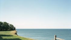 a bench sitting on top of a grass covered hillside next to the ocean and trees