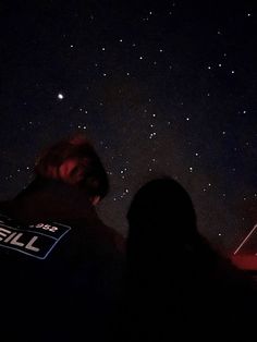 two people are looking up at the stars in the night sky with their backs turned to the camera