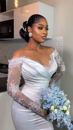 a woman in a white dress holding a bouquet of blue flowers and wearing an off the shoulder wedding dress