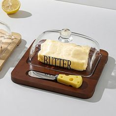 a cutting board topped with butter next to a glass container filled with cheese and two slices of lemon