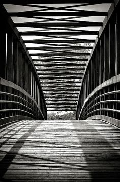 a black and white photo of a bridge with shadows on the ground, taken from below