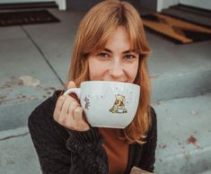 a woman is holding a coffee cup up to her face while sitting on the steps