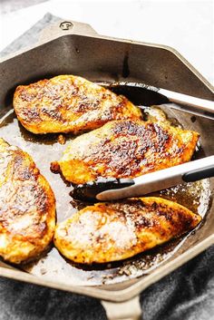 four pieces of chicken cooking in a skillet with tongs on the side,