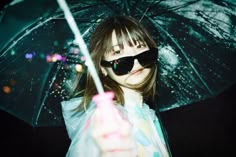 a young woman holding an umbrella in the rain with her eyes closed and wearing sunglasses