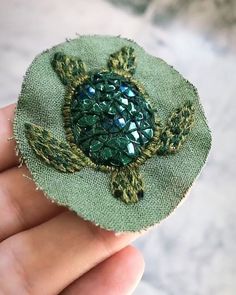 a hand holding a small green brooch with sequins on it's back