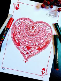 a card with a heart on it surrounded by crayons and markers next to some pens