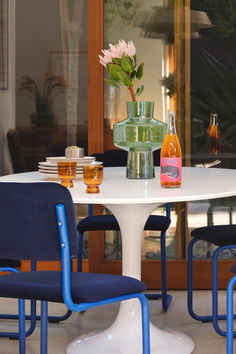 a white table topped with blue chairs and a vase filled with flowers on top of it