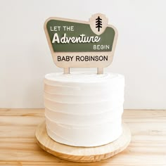 a cake that is sitting on top of a wooden stand with a sign saying let the adventure begin