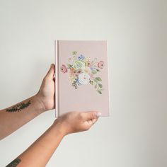 a person holding up a pink book with flowers on the front and back cover in their hands