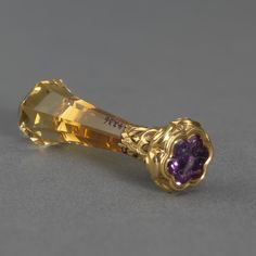 a yellow gold and amethyst colored jeweled object on a gray table top