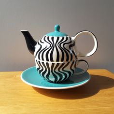 a black and white teapot sitting on top of a blue plate next to a cup