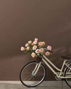 a bicycle with flowers in the basket parked next to a brown wall and wooden floor