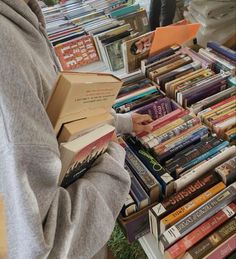 a person standing in front of a table filled with books and holding a box full of books