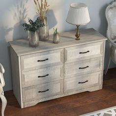 a white dresser sitting on top of a wooden floor next to a lamp and chair