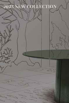 a green table sitting in front of a wall with trees on it and the words new collection