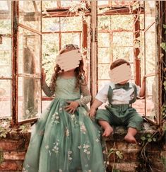 two young children sitting on a window sill with paper taped to their faces in front of them